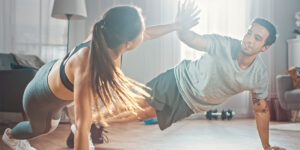 Couple engaging in a fun workout session at home, performing push-up variations with enthusiasm and teamwork in a bright, modern living space.