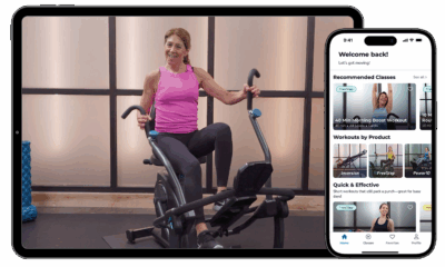 Woman demonstrating a workout on an exercise machine, with a tablet displaying Teeter Move app features and recommended classes for effective home workouts.