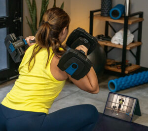 Person watching Teeter Move on tablet while working out with ProFlex 432 Dumbbells