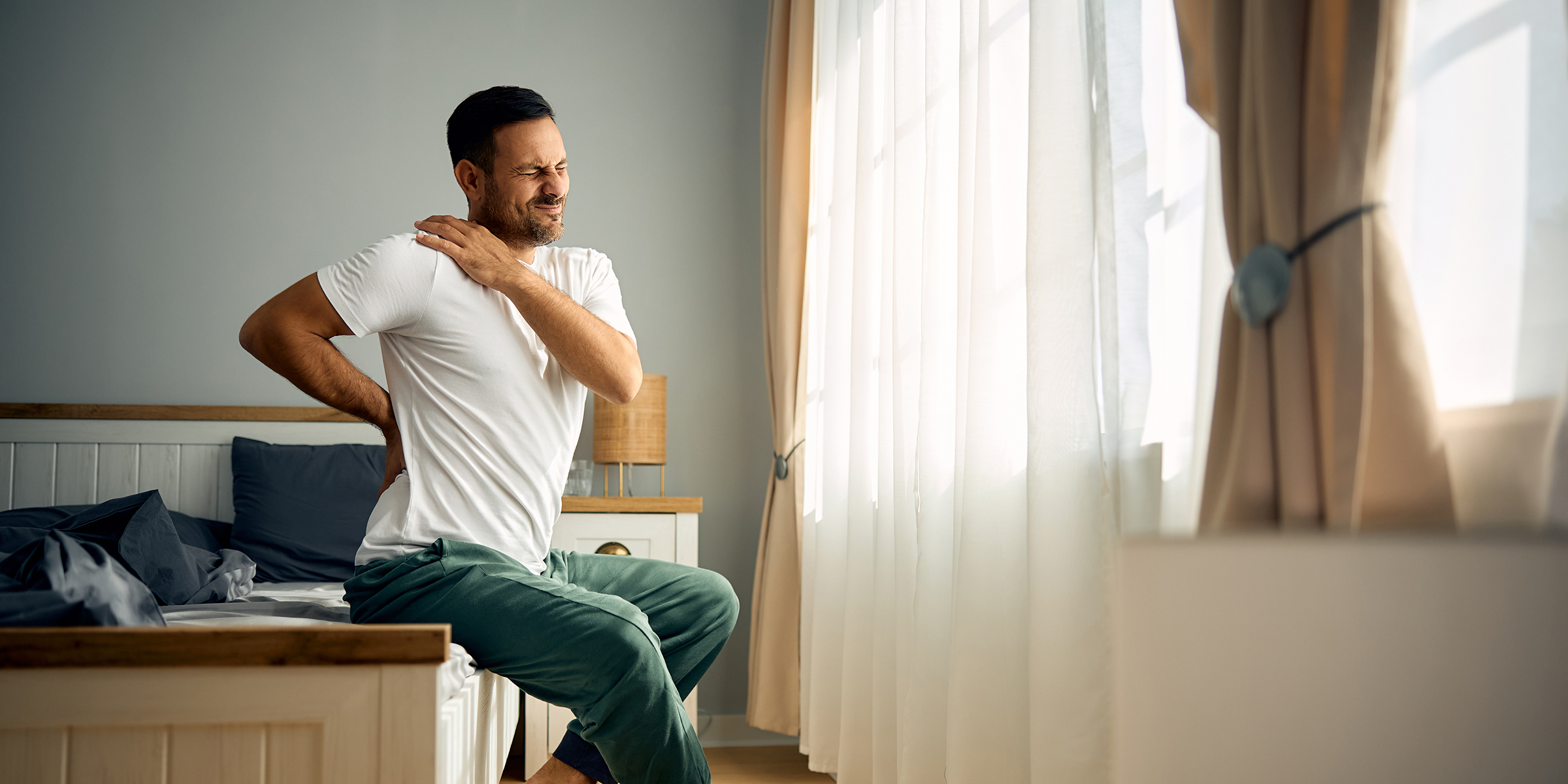 adult man holding his back and shoulder in pain after waking up in morning.