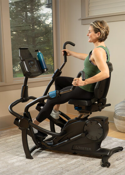 A woman is exercising on a Teeter FreeStep in a bedroom room setting.