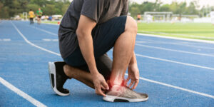 A man crouches on a running track, adjusting his shoe laces in preparation for exercise