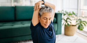 An older woman extends her arms in a spacious living room, showcasing a moment of exercise and self-care.