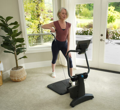 A woman exercises with a FitForm Home Gym in a bright room with large windows.