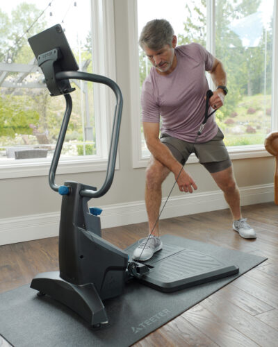 In a living room, a man uses a Teeter TitForm home gym for a single arm row exercise.