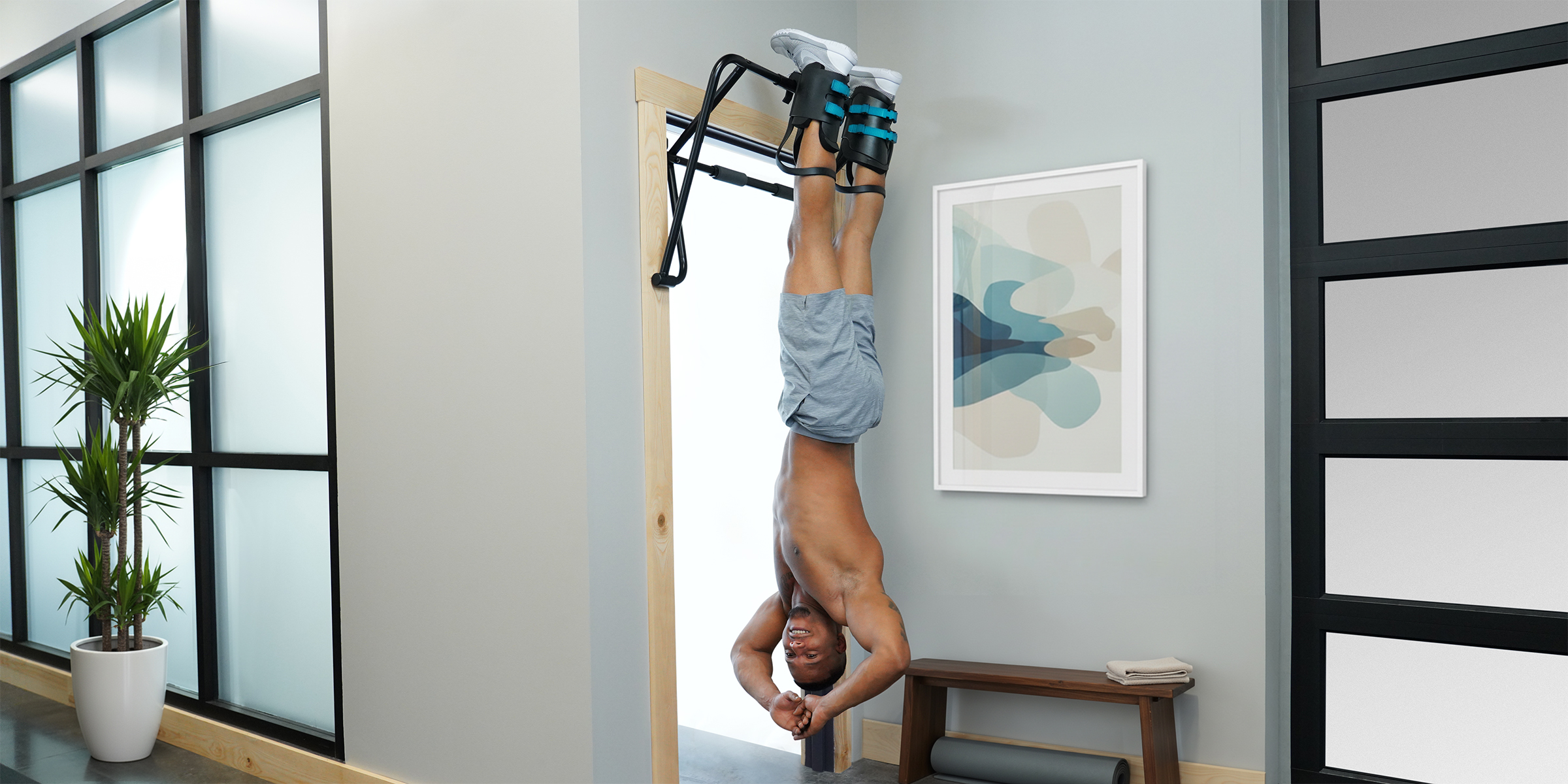 A man hanging upside down from a wall in a room, using Teeter Gravity Boots for inversion therapy.