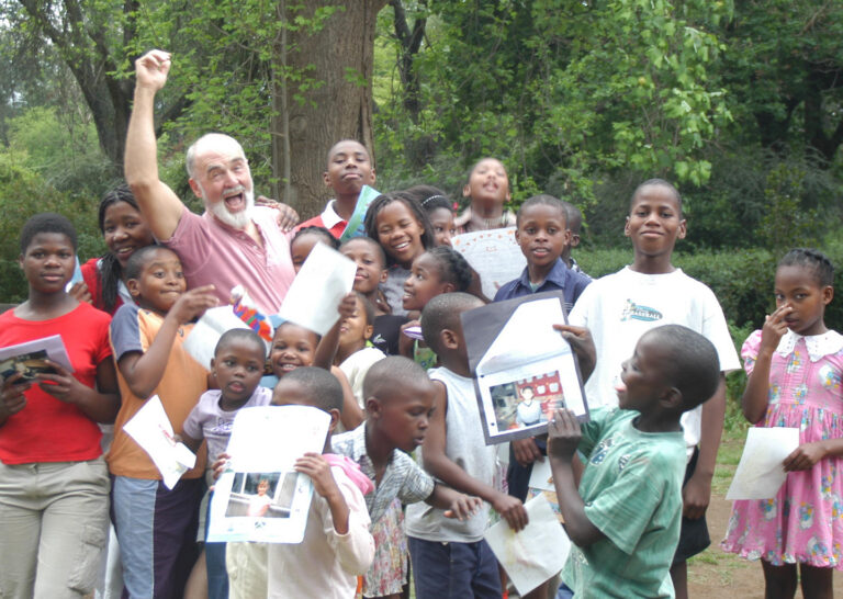 Roger Teeter with a group of children during a community visit, smiling and celebrating together