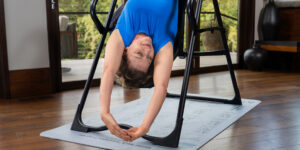 Woman inverting with Teeter FitSpine Inversion table on an inversion program mat